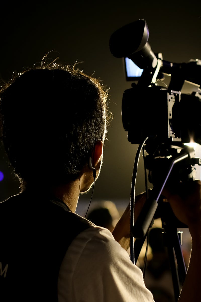A cameraman filming an event outdoors at night with professional equipment, capturing the vibrant atmosphere.